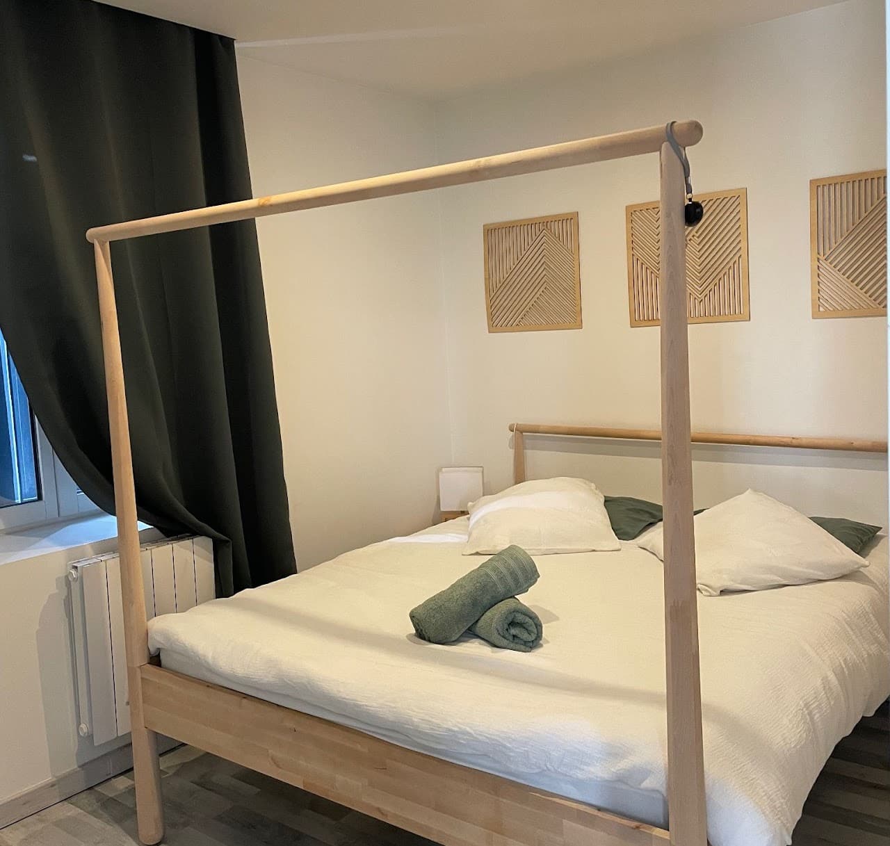 Wooden canopy bed with white bedding and rolled green towels in a minimalist bedroom.